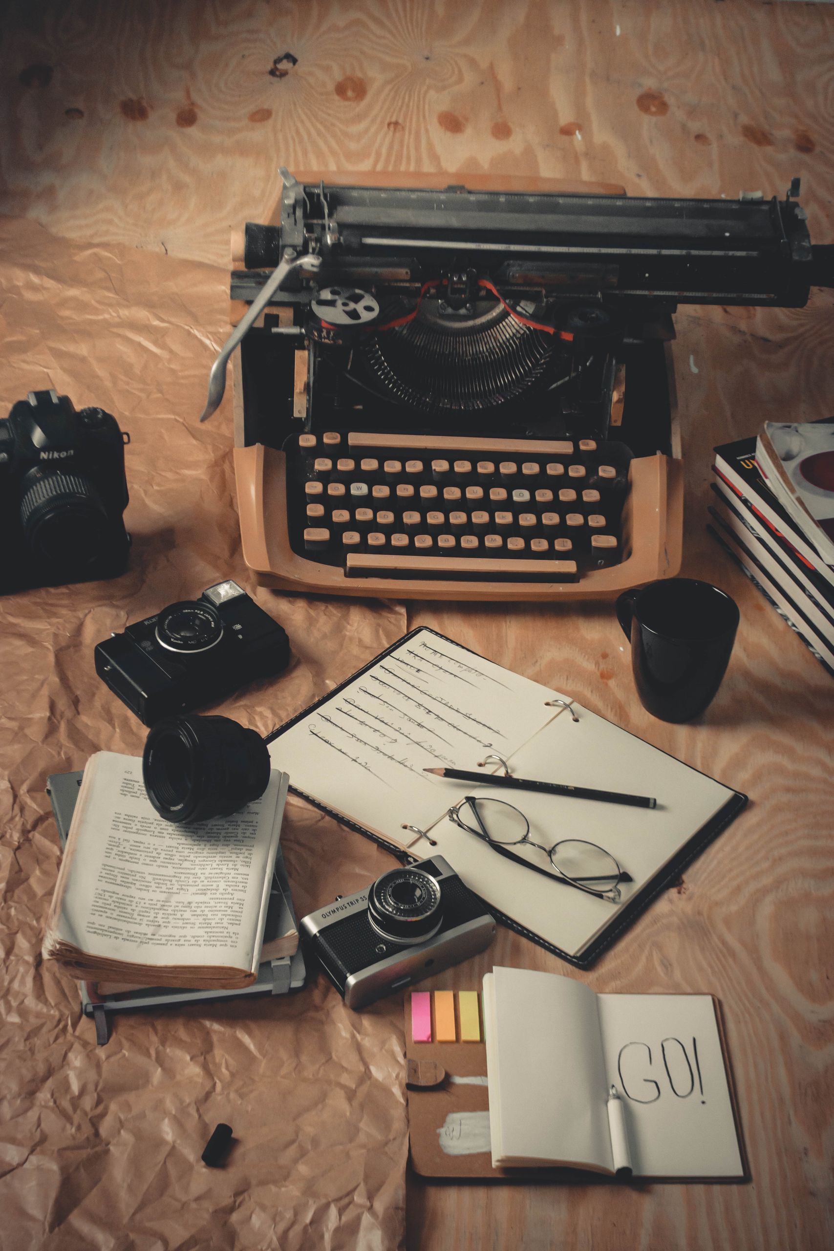 Nostalgic scene with a vintage typewriter, cameras, books, and writing tools on a wooden surface.